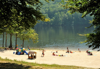 Sandy beach with playground and lake, shaded by trees at Flower Camping La Plage in Nouvelle-Aquitaine, France.