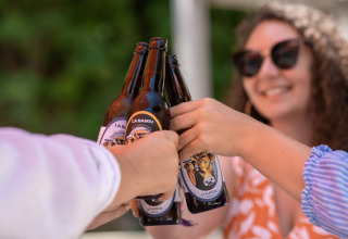Menschen stoßen mit Bierflaschen an und genießen die Sonne bei Flower Camping La Plage in Nouvelle-Aquitaine, Frankreich.