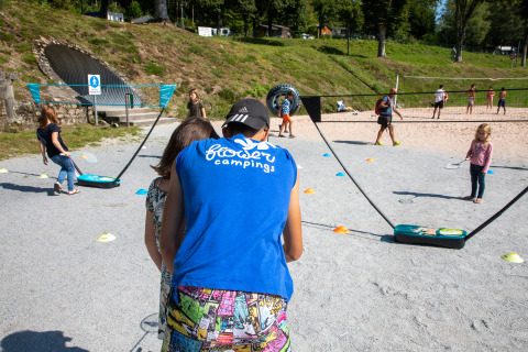 Niños y adultos juegan al bádminton al aire libre bajo el sol en Flower Camping La Plage, Nouvelle-Aquitaine, Francia.