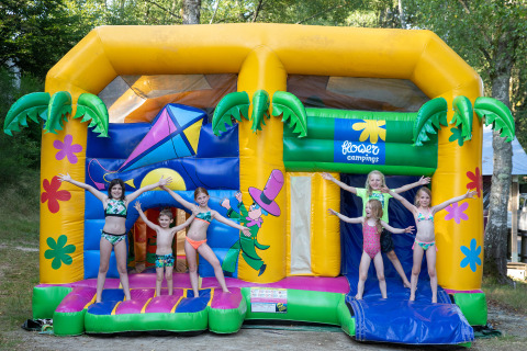 Kinderen in badkleding spelen op een kleurrijk springkasteel bij Flower Camping La Plage in Nouvelle-Aquitaine, Frankrijk.