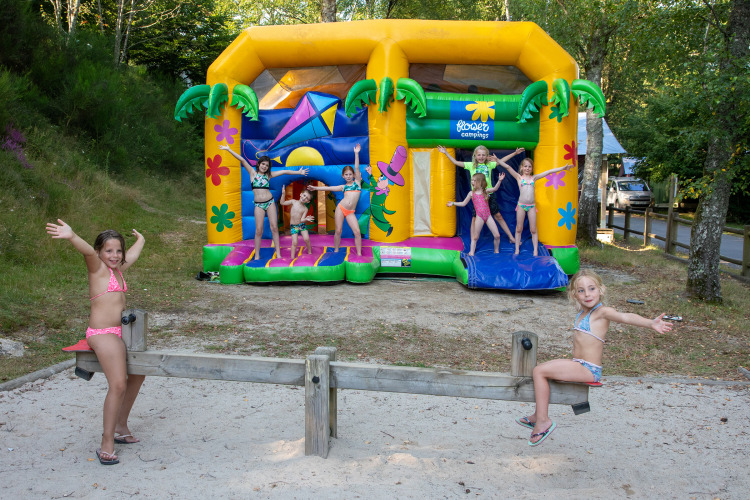 Children playing on a seesaw and bouncy castle at Flower Camping La Plage, Nouvelle-Aquitaine, France.