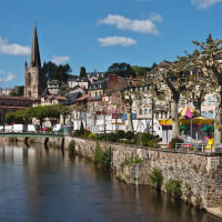 Udsigt over floden, farverige huse og en kirke i Treignac-sur-Vézère, Nouvelle-Aquitaine, Frankrig.