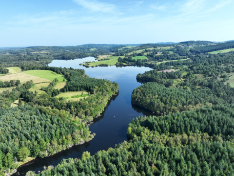 Vista aerea di un lago circondato da foreste e campi verdi a Flower Camping La Plage, Nouvelle-Aquitaine, Francia.