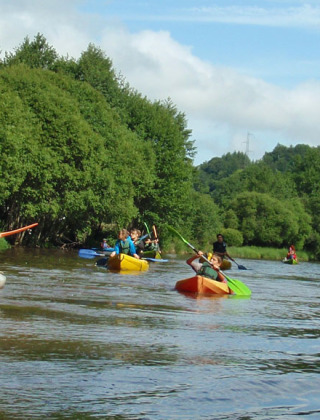 En gruppe mennesker padler i kajakker på en flod omgivet af grønne træer nær Treignac-sur-Vézère, Frankrig.