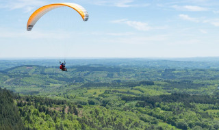 Paraglider flyver over det frodige og bakkede landskab nær Treignac-sur-Vézère i Nouvelle-Aquitaine, Frankrig.
