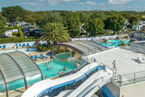 Parc de vacances en Bretagne, France, avec piscine couverte, toboggans aquatiques et vacanciers détendus.