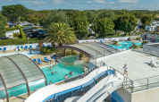 Feriepark i Bretagne, Frankrig, med overdækket swimmingpool, vandrutsjebaner og gæster der nyder solen.