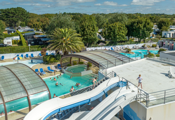 Feriepark i Bretagne, Frankrig, med overdækket swimmingpool, vandrutsjebaner og gæster der nyder solen.