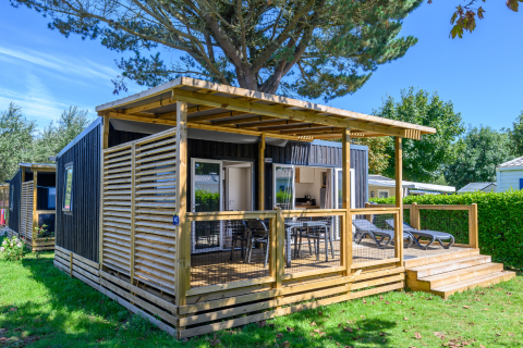 Moderne chalet met overdekt houten terras en ligstoelen op Flower Camping Cap Finistère in Bretagne, Frankrijk.