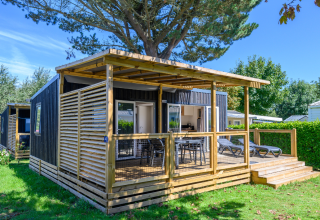 Moderne hytte med overdækket terrasse og liggestole i Flower Camping Cap Finistère, feriepark i Bretagne, Frankrig.