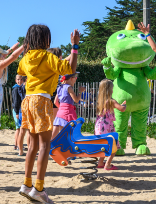 Kinderen spelen en springen in het zand met een groot groen mascotte bij Flower Camping Cap Finistère.
