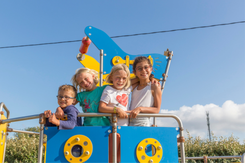 Cuatro niños sonrientes posan juntos en un parque infantil en Flower Camping Cap Finistère, Bretaña, Francia.