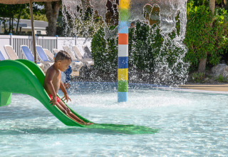 Un bambino scivola su uno scivolo verde in una piscina con fontana in un villaggio turistico in Bretagna, Francia.