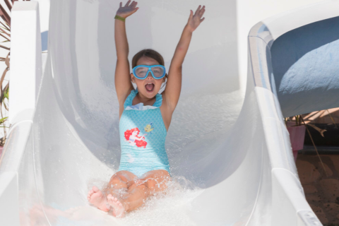 Een kind met zwembril glijdt enthousiast van een waterglijbaan op een vakantiepark in Bretagne, Frankrijk.