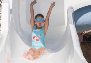 Een kind met zwembril glijdt enthousiast van een waterglijbaan op een vakantiepark in Bretagne, Frankrijk.