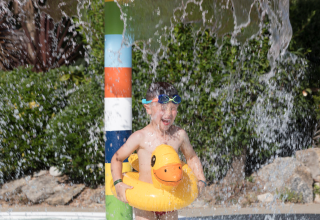 Kind met eend-zwemband en duikbril onder waterval in waterpark bij Flower Camping Cap Finistère, Bretagne.