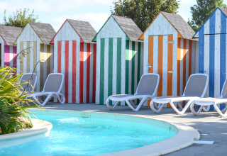 Gekleurde strandhokjes en ligstoelen bij het zwembad op Flower Camping Cap Finistère in Bretagne, Frankrijk.