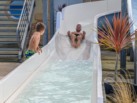 Un homme glisse sur un toboggan aquatique pendant qu’un garçon attend à la sortie au Flower Camping Cap Finistère.