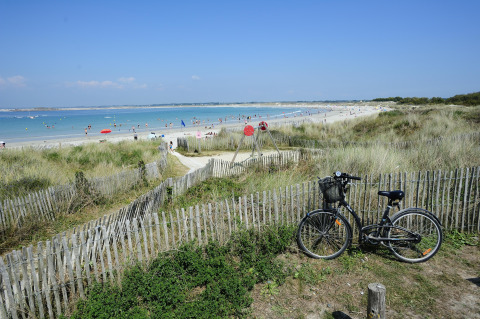 Fiets geparkeerd bij een houten hek met uitzicht op het strand bij Flower Camping Cap Finistère, Bretagne.