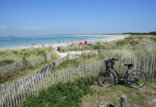 Fiets geparkeerd bij een houten hek met uitzicht op het strand bij Flower Camping Cap Finistère, Bretagne.