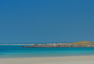 Strandscene ved Flower Camping Cap Finistère i Bretagne, Frankrig, med klart blåt hav og folk på sandet.
