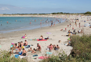 Spiaggia affollata al Flower Camping Cap Finistère in Bretagna, Francia, con persone che nuotano e si rilassano.