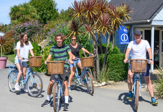 Four people happily riding bikes in front of the reception at Flower Camping Cap Finistère, Brittany, France.
