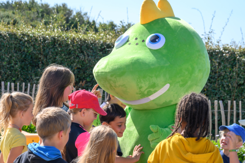 Niños juegan y saludan a una gran mascota verde en Flower Camping Cap Finistère en Bretaña, Francia.