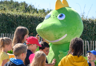 Niños juegan y saludan a una gran mascota verde en Flower Camping Cap Finistère en Bretaña, Francia.