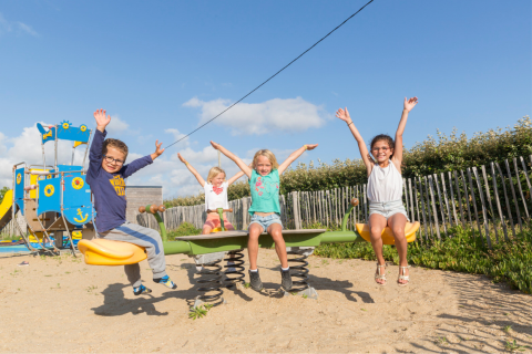 Niños juegan en un balancín bajo el cielo azul en Flower Camping Cap Finistère en Bretaña, Francia.