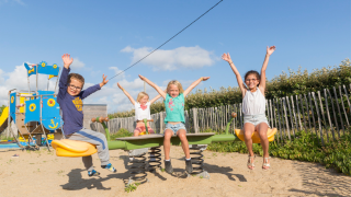 Des enfants jouent sur une balançoire sous un ciel bleu au Flower Camping Cap Finistère en Bretagne, France.