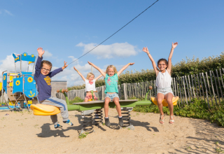Kinderen spelen op een wip onder een blauwe lucht op Flower Camping Cap Finistère in Bretagne, Frankrijk.