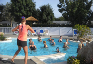 En gruppe mennesker deltager i vandgymnastik i en udendørs pool omgivet af træer på en feriepark.