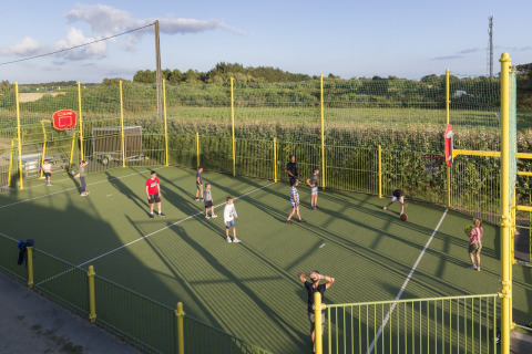 Children play basketball on an outdoor fenced court at Flower Camping Cap Finistère in Brittany, France.