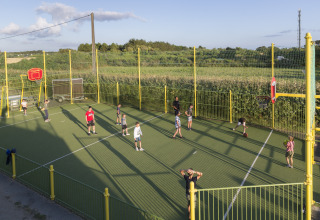 Børn leger basketball på en udendørs bane med gult hegn i Flower Camping Cap Finistère i Bretagne.