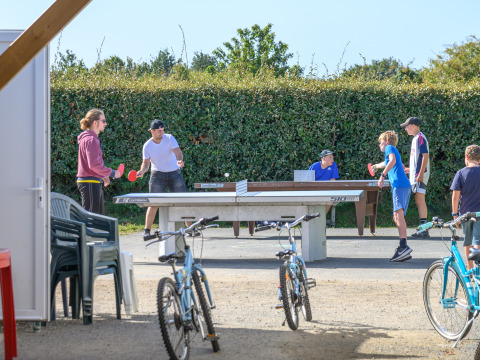 Personas y niños juegan al tenis de mesa al aire libre entre bicicletas en Flower Camping Cap Finistère, Bretaña, Francia.