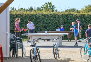 Menschen und Kinder spielen draußen Tischtennis zwischen Fahrrädern im Flower Camping Cap Finistère, Bretagne.