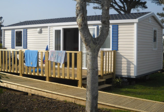 Mobilhome med træterrasse og gangbro i et grønt ferieområde på Flower Camping Cap Finistère, Bretagne, Frankrig.