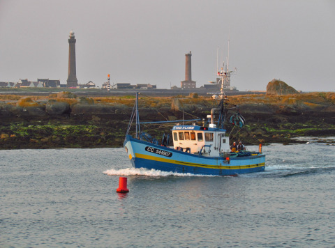 Fiskerbåd sejler ved Flower Camping Cap Finistère i Bretagne, Frankrig, med fyrtårne i baggrunden.