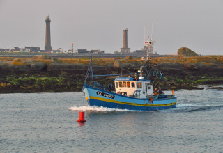 Fishing boat sails by Flower Camping Cap Finistère in Brittany, France, with lighthouses visible on the shore.