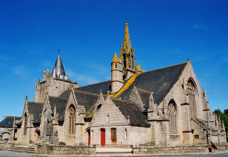 Stenbygget kirke med spir og detaljerede vinduer under en klar blå himmel i Bretagne, Frankrig.
