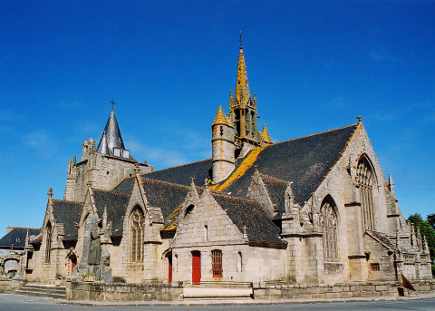 Stenen kerk met hoge toren en gotische ramen onder een blauwe lucht in Bretagne, Frankrijk.