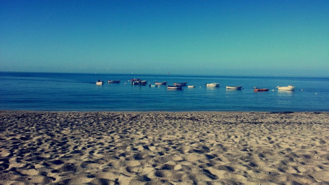 Zandstrand en boten voor de kust bij Flower Camping Cap Finistère, een vakantiepark in Bretagne, Frankrijk.