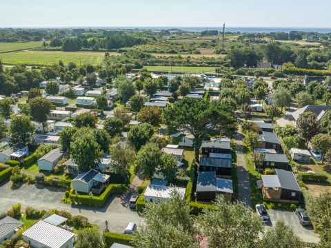 Aerial view of Flower Camping Cap Finistère holiday park in Brittany, France, with lodges, greenery and sea view.