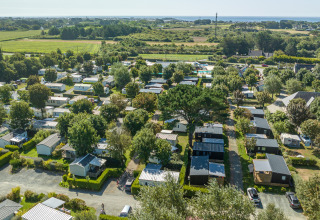 Luftfoto af Flower Camping Cap Finistère feriepark i Bretagne, Frankrig, med hytter, grønt og udsigt til havet.