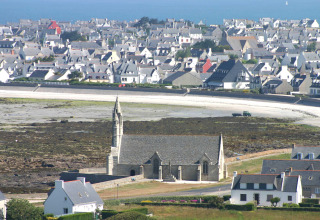 Udsigt over ferieparken Flower Camping Cap Finistère i Bretagne, Frankrig, med kirke og kystby i baggrunden.