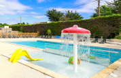 Piscina all’aperto con zona giochi d’acqua per bambini e scivolo giallo al Flower Camping Le Vieux Moulin, Bretagna, Francia.