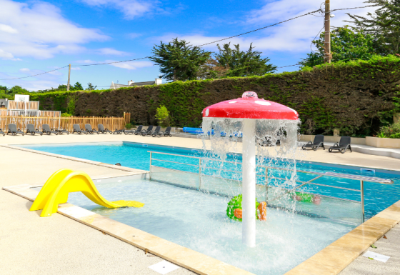 Outdoor swimming pool with children’s splash play area and yellow slide at Flower Camping Le Vieux Moulin, Brittany, France.