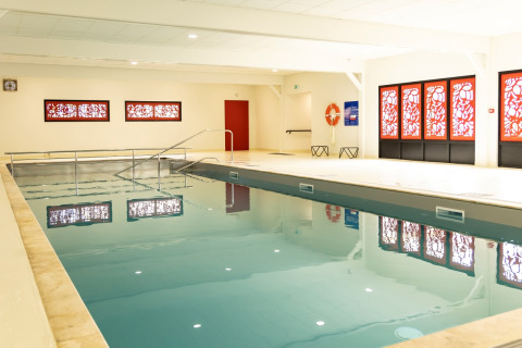 Indoor swimming pool with red decorative windows at Flower Camping Le Vieux Moulin, Brittany, France holiday park.