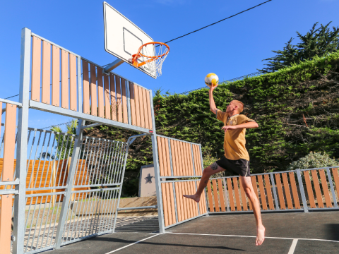 Mann spielt Basketball im Ferienpark Flower Camping Le Vieux Moulin in der Bretagne, Frankreich, bei Sonne.